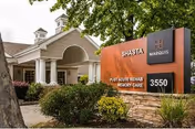 Exterior view of Marquis Care At Shasta facility showing the entrance with white columns and a large sign displaying 'Shasta', 'Post Acute Rehab Memory Care', and the address number 3550, surrounded by greenery and trees.