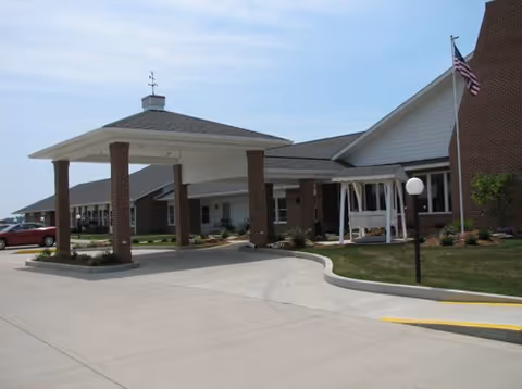 Front view of a brick senior living facility with a covered entrance and landscaped lawn.