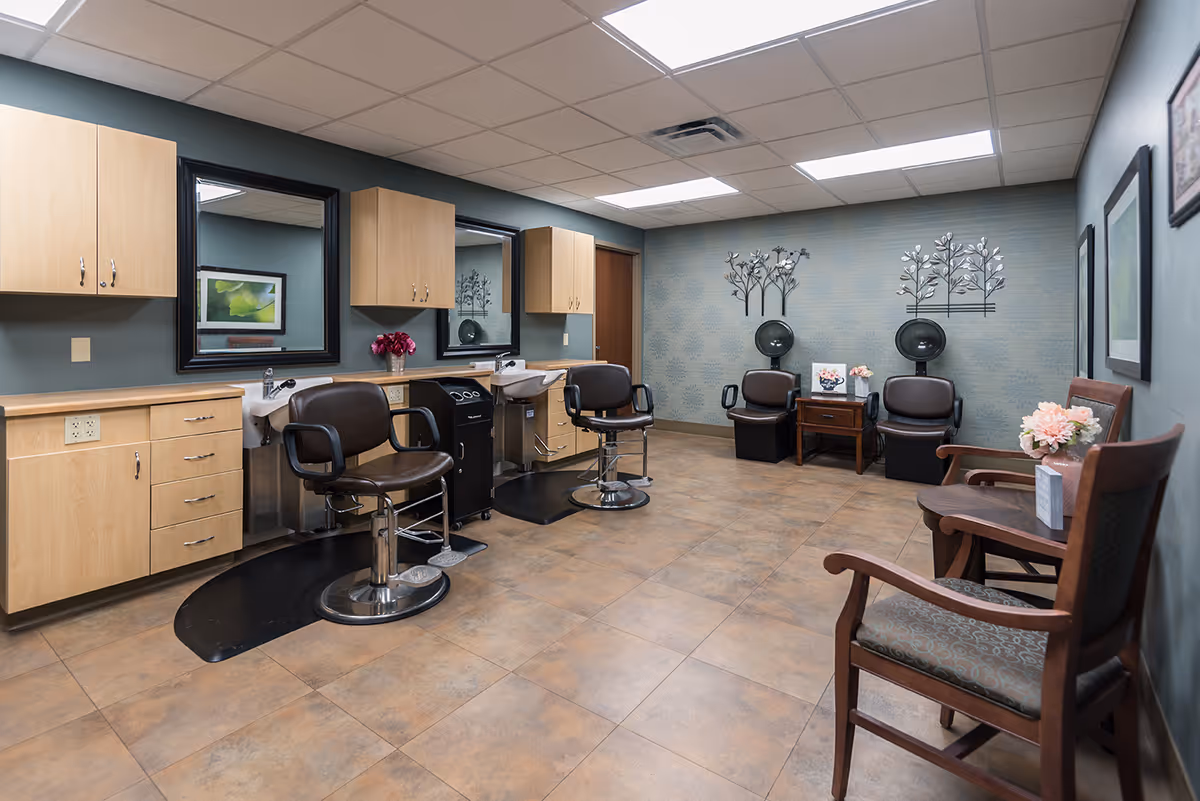 Well-lit salon room with styling stations, shampoo sinks, hooded dryers and waiting chairs.