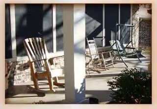 Outdoor porch with rocking chairs and a bench along a building.
