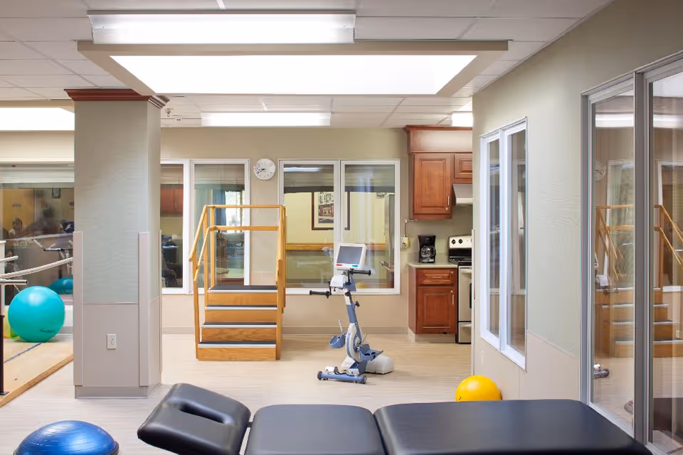 Physical therapy room with an exercise bike, treatment table, therapy stairs, and exercise balls.