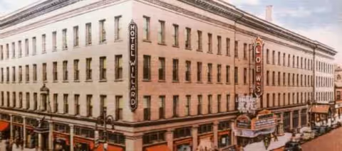 Exterior view of a large brick corner building with vertical hotel signs along the street.