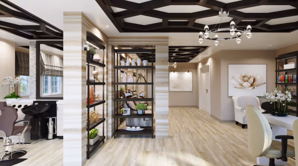 A modern interior space with light wood flooring and beige walls. The ceiling features dark geometric beams with recessed lighting and a circular chandelier. On the left, there is a salon area with a hair washing station and a styling chair. In the center, black metal shelving units display decorative items and plants. On the right, there is a seating area with white armchairs, a white table, and a large floral artwork on the wall. The space is bright with natural light coming through windows with patterned Roman shades.