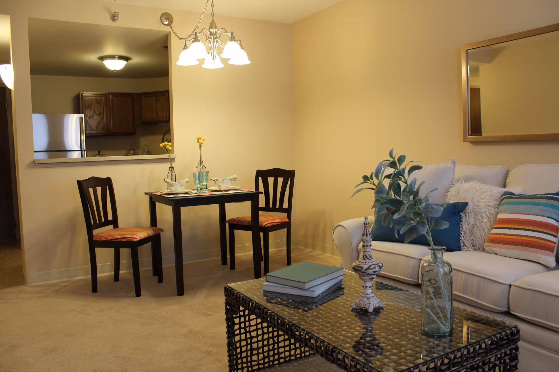 Living room and dining nook with a sofa, coffee table, and two-seat dining table by a kitchen pass-through.