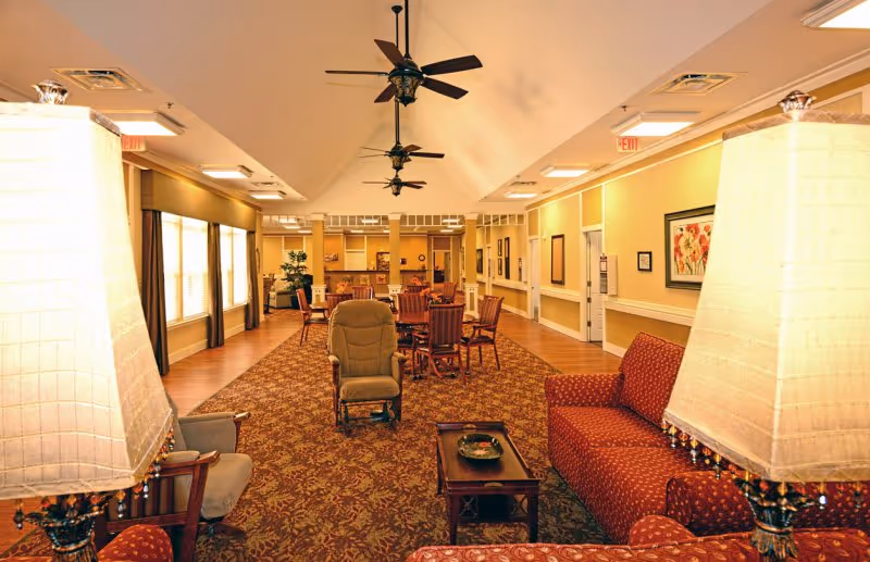 A spacious lobby area featuring comfortable seating, ceiling fans, and large windows. The decor includes warm colors and artwork on the walls, creating a welcoming atmosphere.