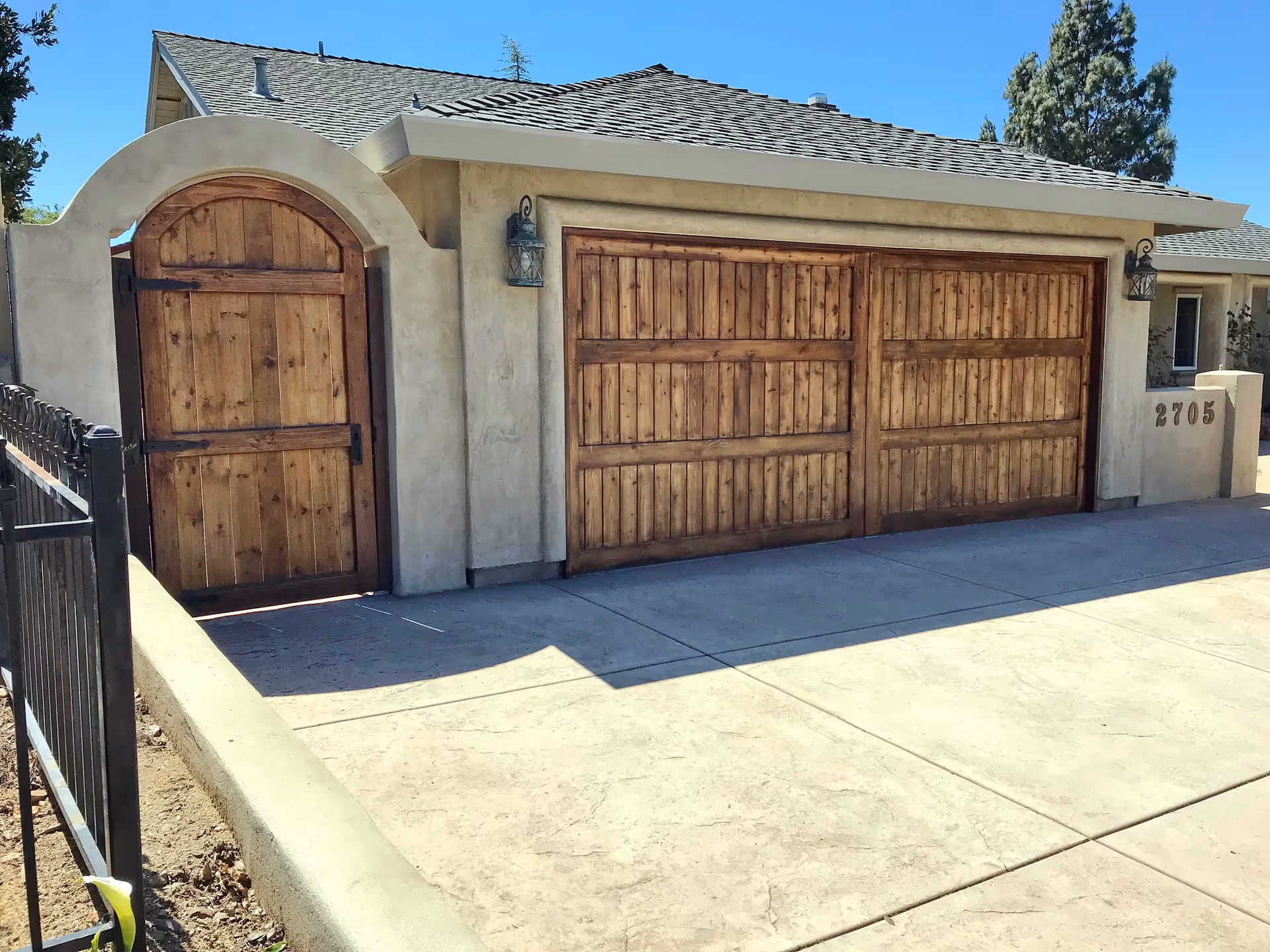 Front exterior of a house featuring a wooden double garage door and an arched wooden gate.