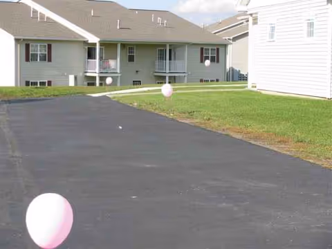 Front view of a senior living complex with balconies, a paved driveway, and balloons.