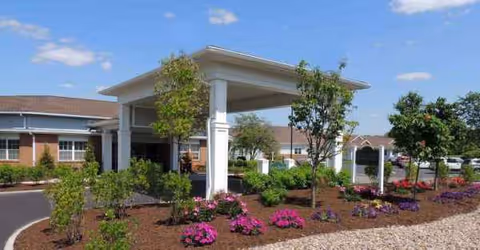 The entrance of a retirement community with a covered drop-off and landscaped front.