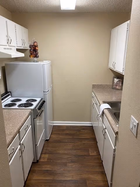 Narrow galley kitchen with white cabinets, electric stove and refrigerator, laminate countertops and wood-look flooring.