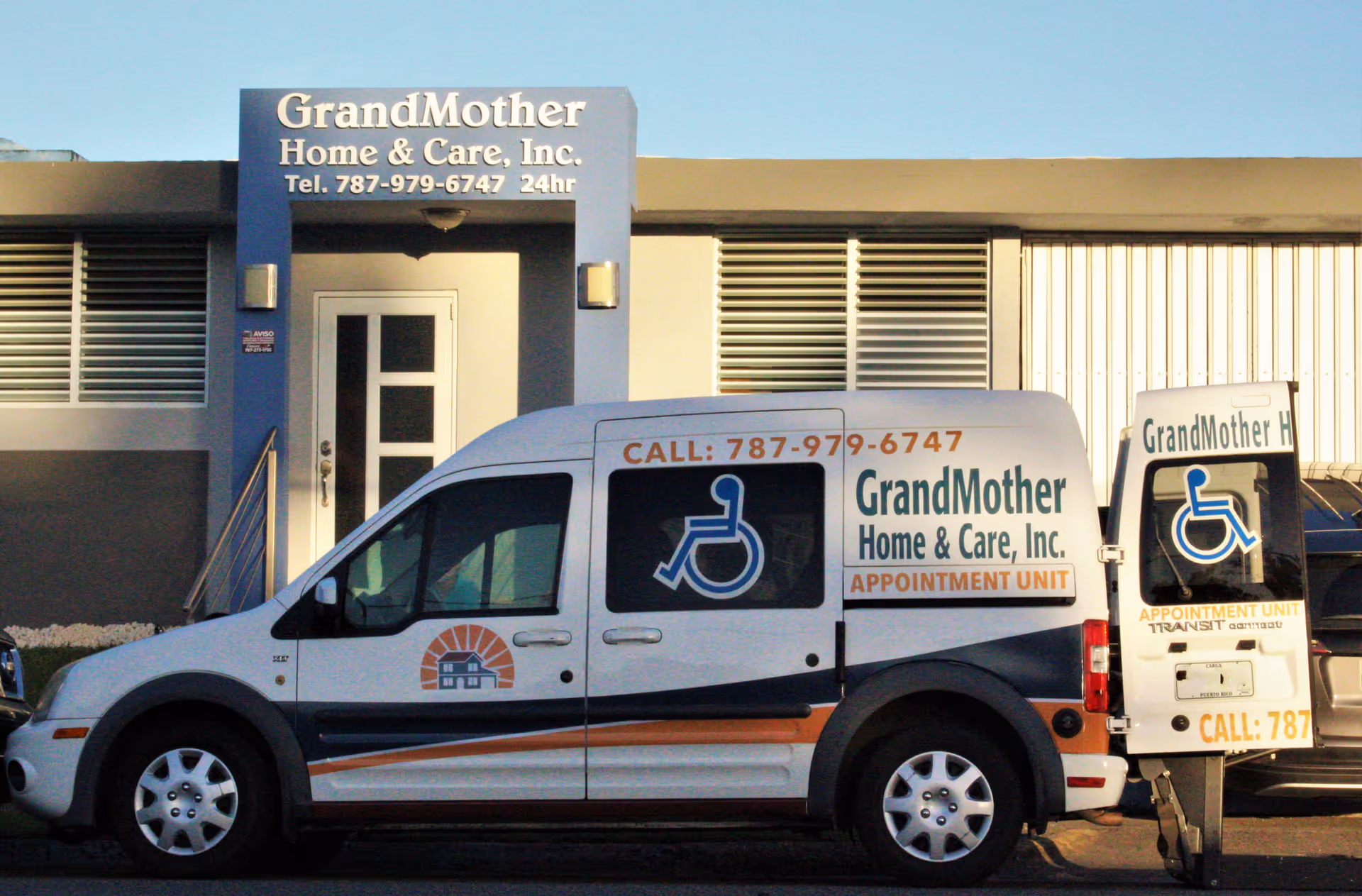 A white accessible van with GrandMother Home & Care signage and wheelchair symbols parked in front of the GrandMother Home & Care, Inc. building and entrance.