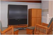 Small living room with a large TV, wooden chairs and cabinets.