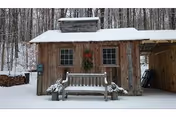 Winter scene of a wooden shed with bench and wreath, snow-covered surroundings.