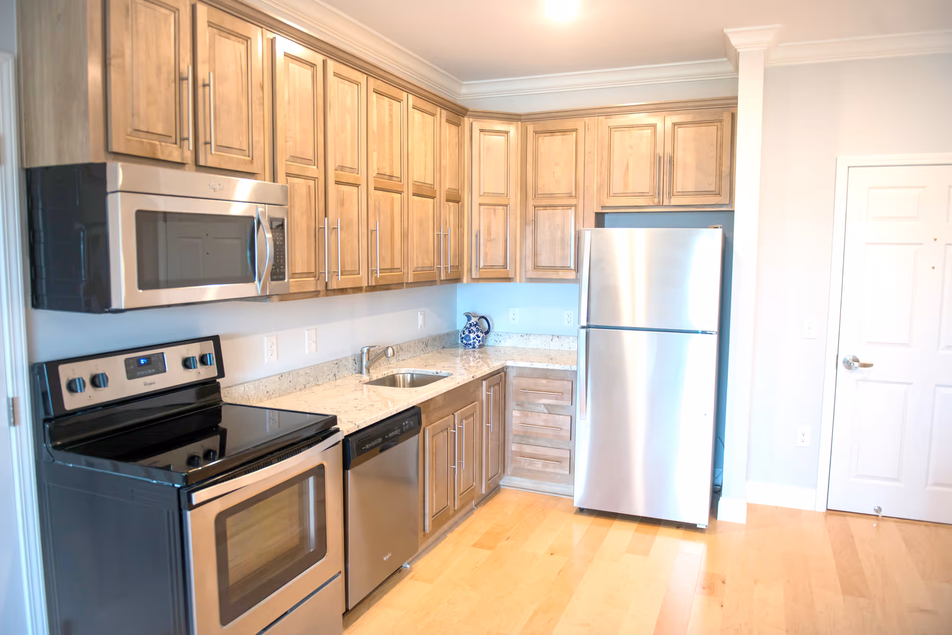 Bright modern kitchen with stainless steel appliances, wooden cabinets, and a granite countertop.