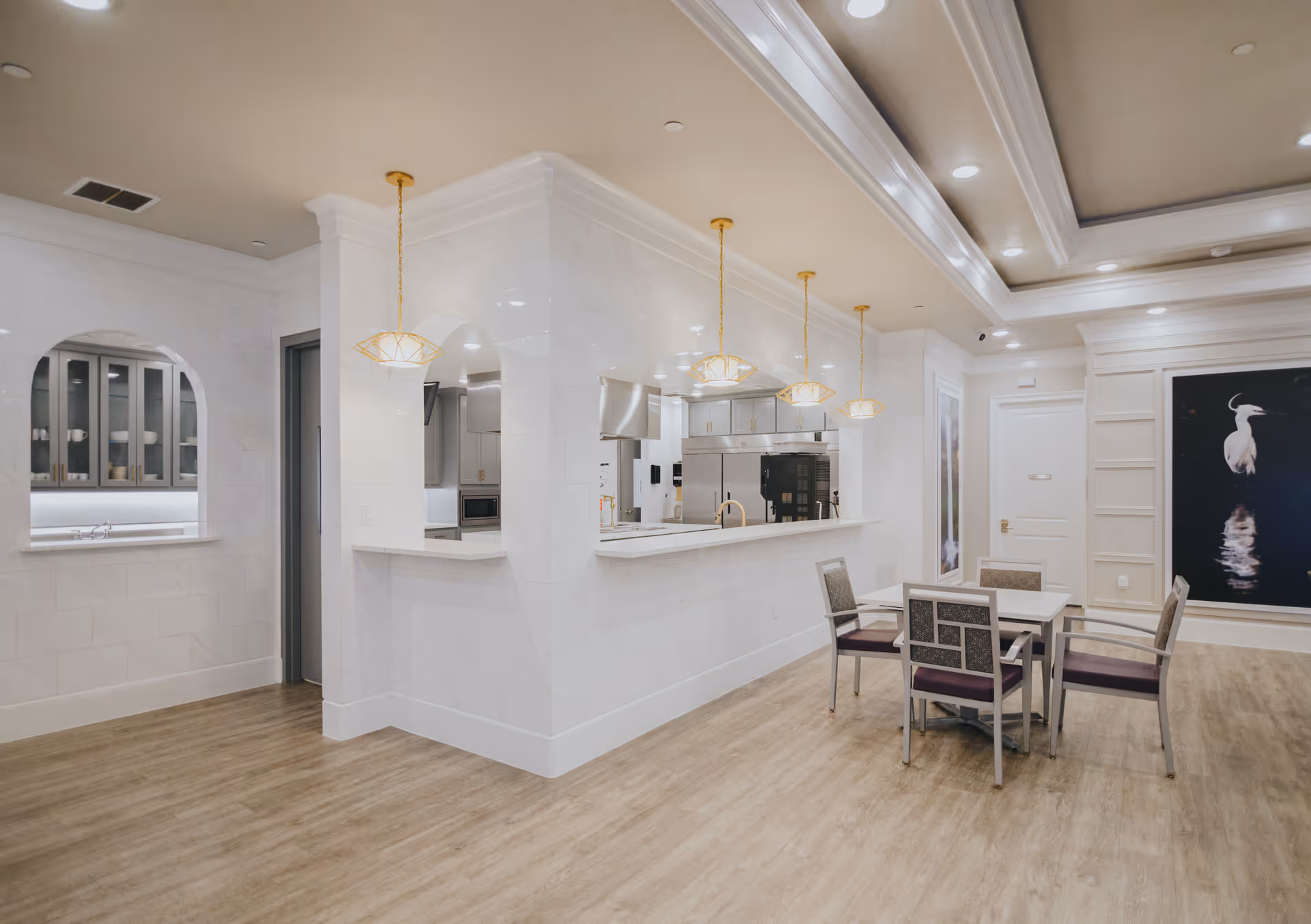 Bright open dining and kitchen area with a serving counter, pendant lights, and a small table with chairs.