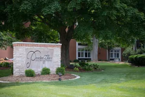 Exterior view of Proctor Place Senior Living with sign and landscaped lawn.