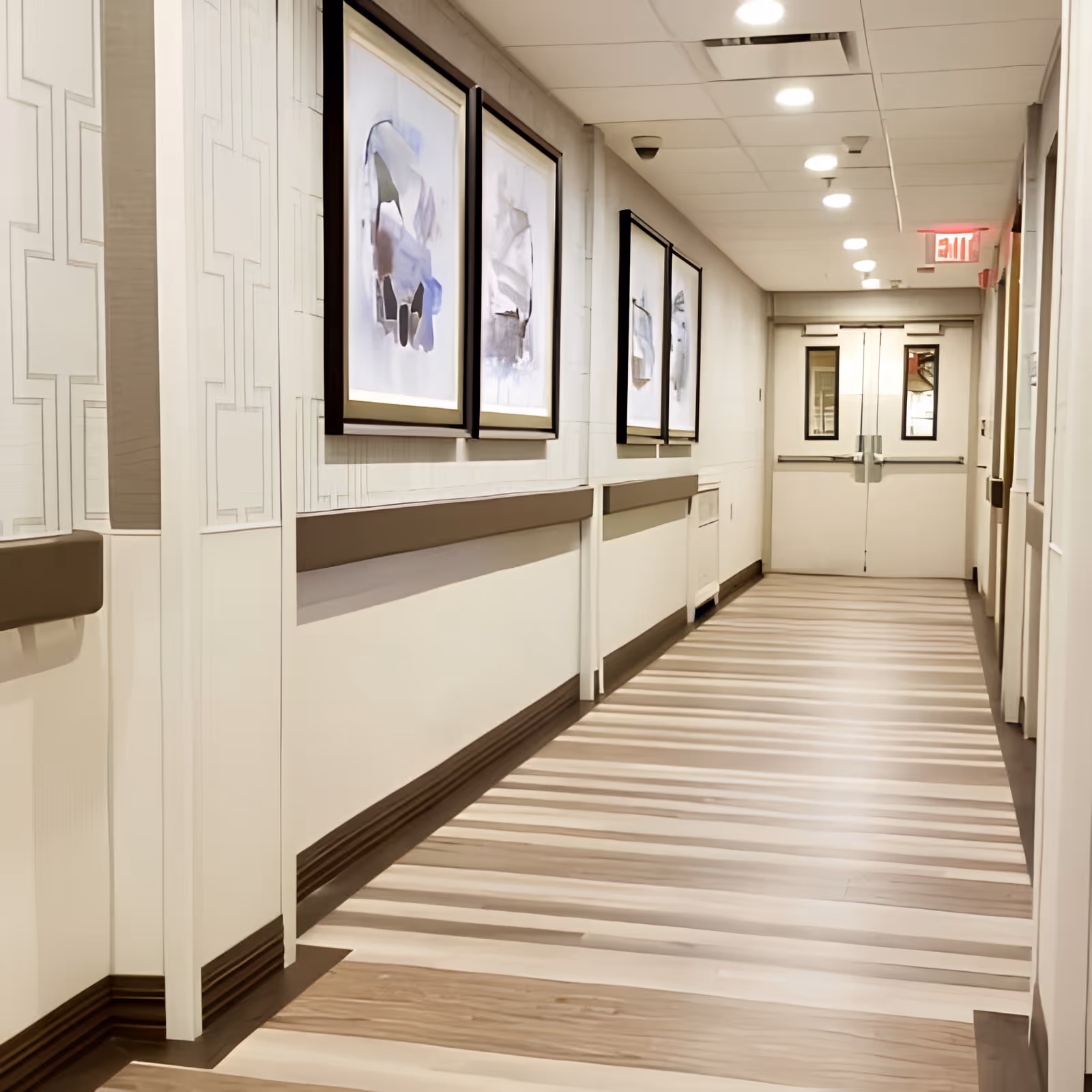 A clean, well-lit interior corridor with framed artwork on the walls and double doors at the far end.