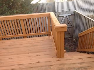 Wooden outdoor deck with railings and stairs leading down to a fenced yard with a wooden gate.