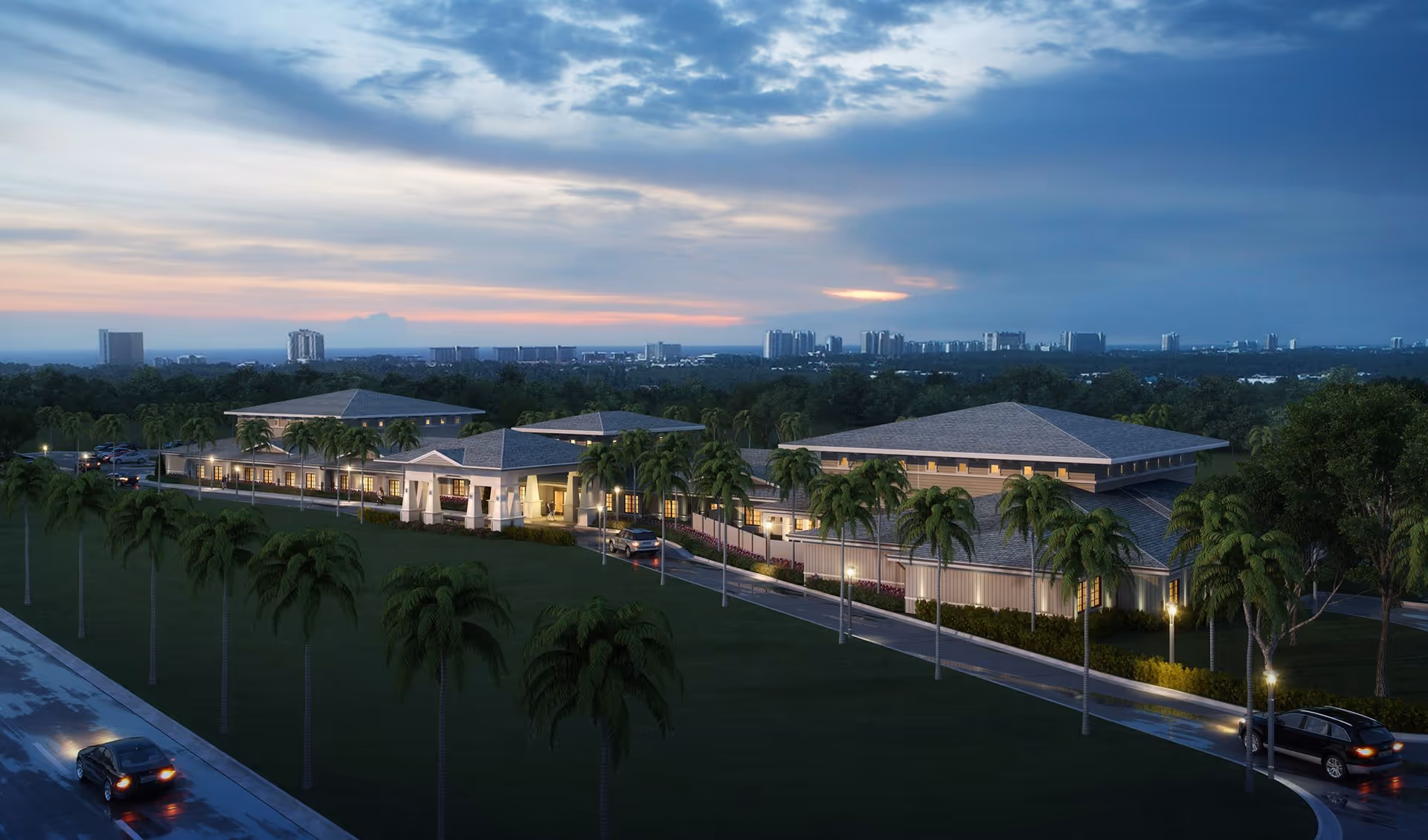 Dusk exterior view of a low-rise senior living complex surrounded by palm trees, a driveway with cars, and a distant skyline.