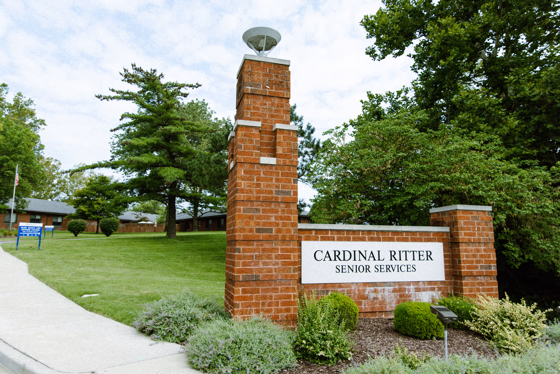 A brick entrance sign for Cardinal Ritter Senior Services sits on a landscaped lawn with trees.