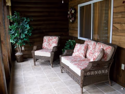 Covered porch with wicker loveseat and chair with floral cushions, potted plants, and a sliding glass door.
