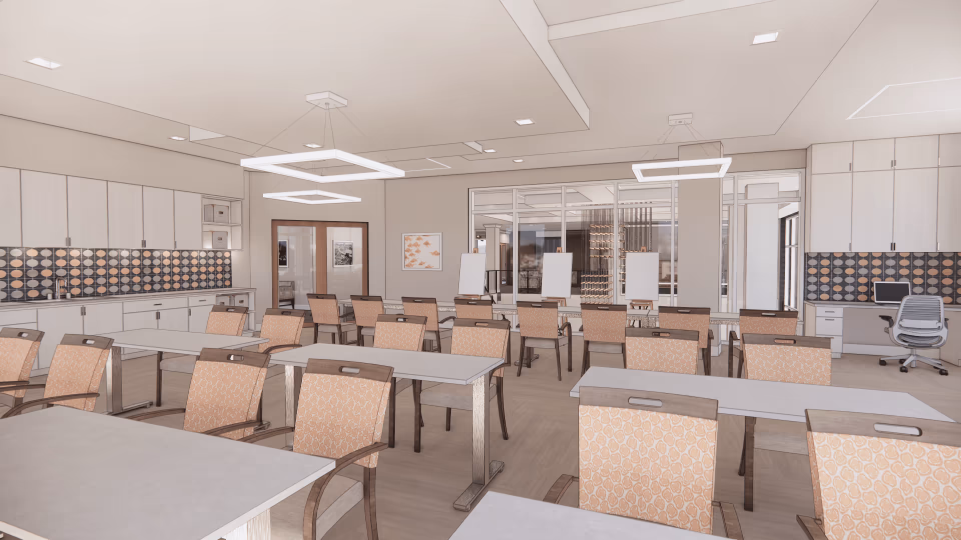 A spacious, well-lit room with multiple tables and chairs arranged in rows, featuring light wood cabinetry along the walls with a patterned backsplash. The room includes modern square pendant lights hanging from the ceiling, a desk with a computer chair on the right side, and several easels with blank canvases near the back glass wall.