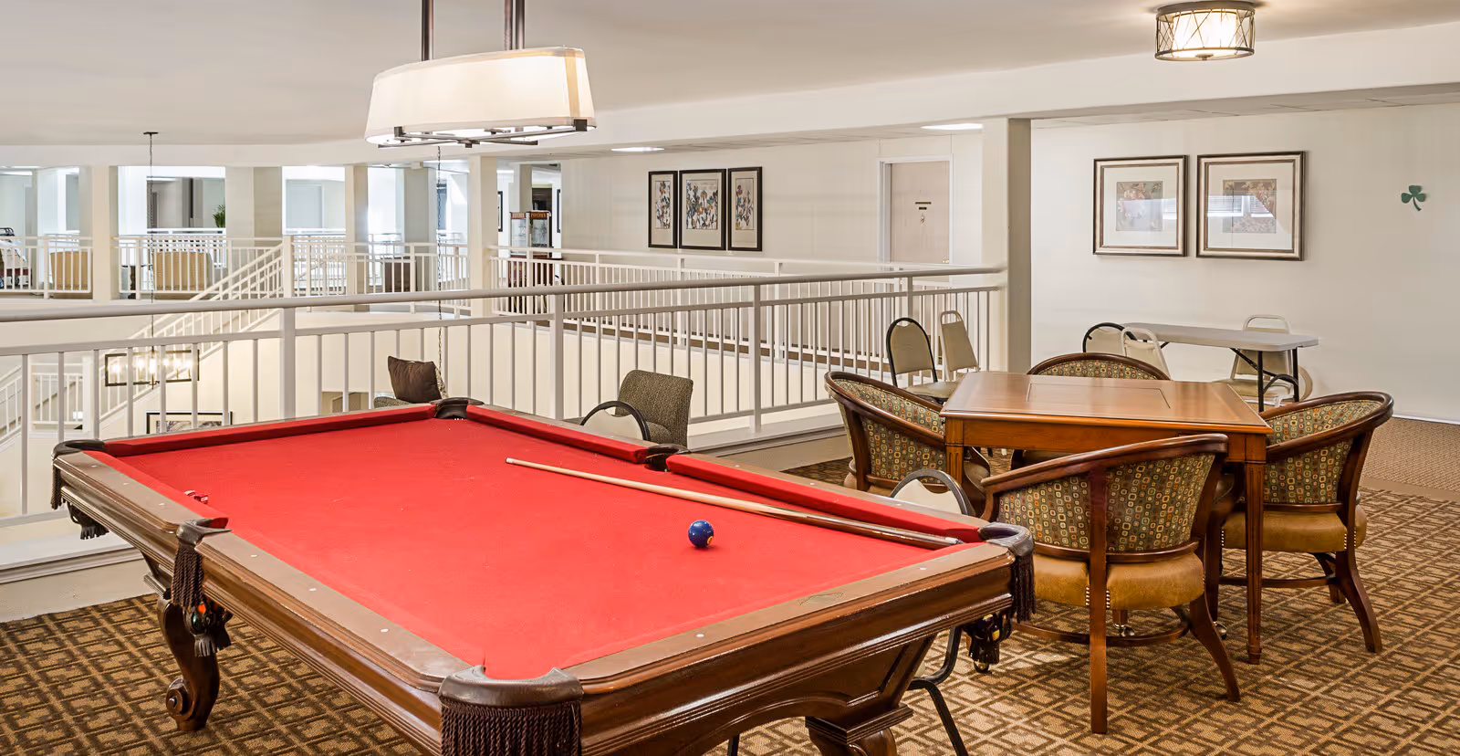 Open indoor common area with a red-felt pool table, seating and card tables overlooking an interior atrium.