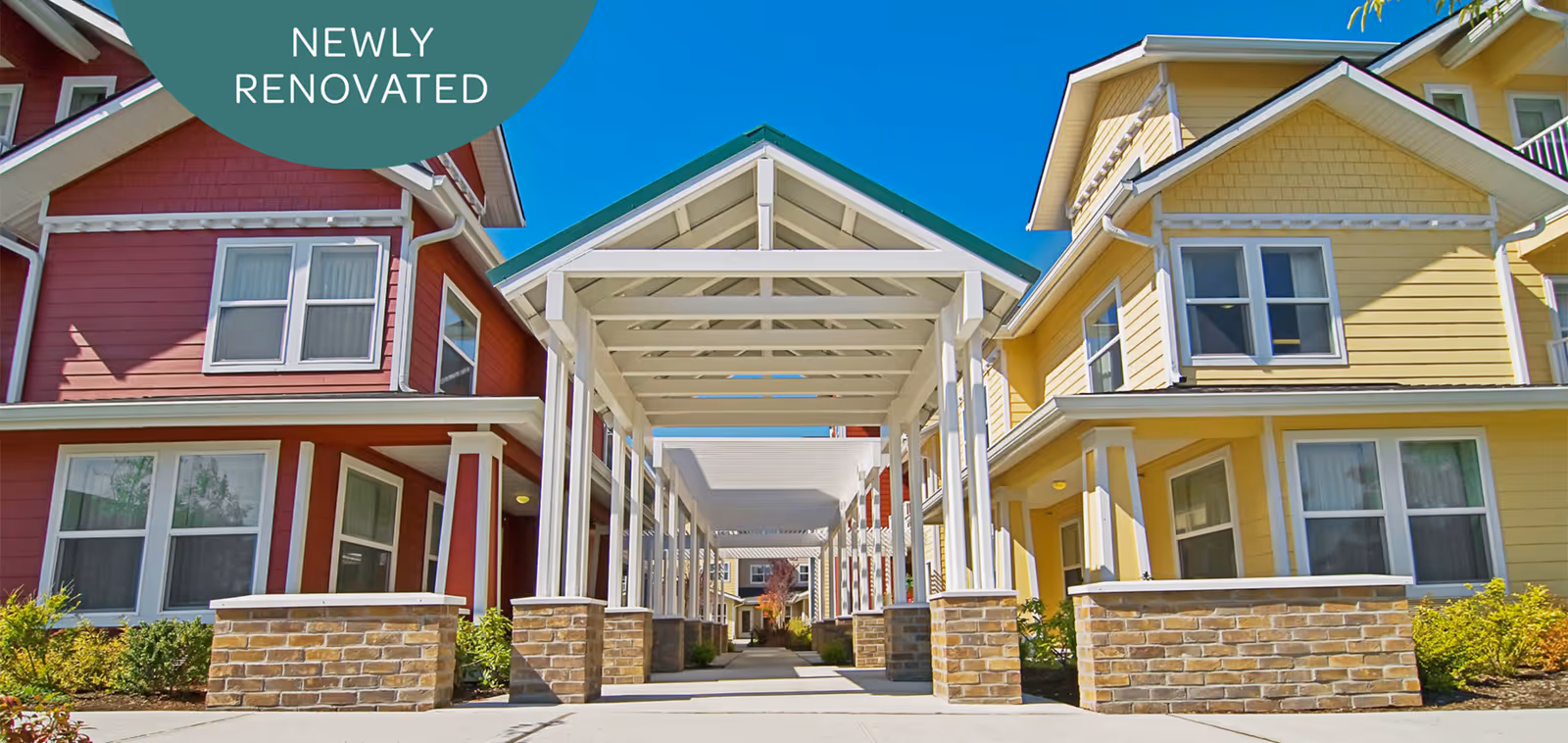 Covered entry walkway between two colorful renovated buildings with red and yellow siding under a blue sky.