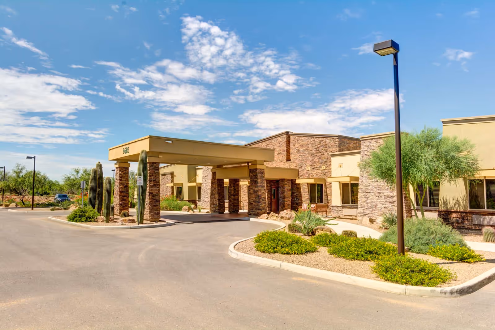 Front entrance of Catalina Springs Memory Care building with a covered porte-cochere, desert landscaping and a clear blue sky.