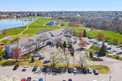 Aerial view of the Vitality Living Elizabethtown building with parked cars, flowering trees, surrounding green space and a nearby lake.