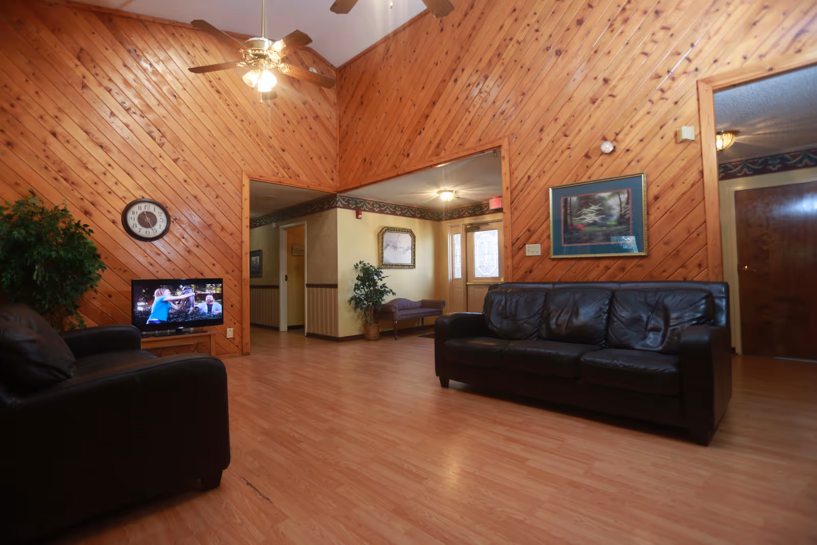 Wood-paneled lounge with leather couches, a television, wall clock, and framed artwork.