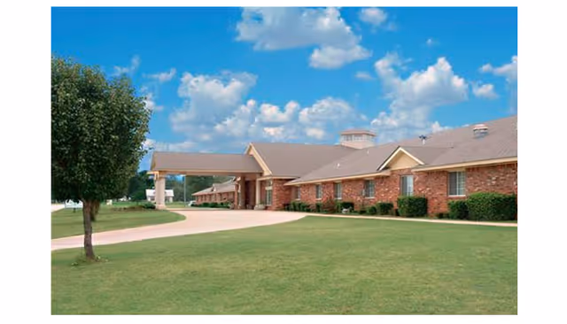 Brick senior living facility with a covered entrance, manicured lawn, and blue sky.