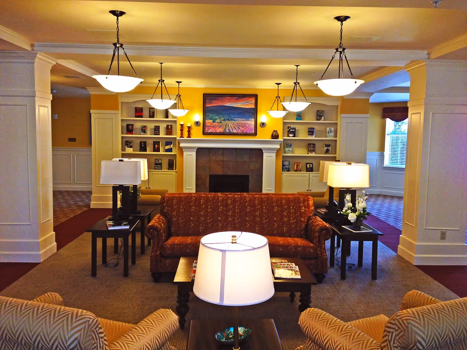 Cozy communal living room with sofas, side tables and lamps facing a fireplace flanked by built-in bookshelves.