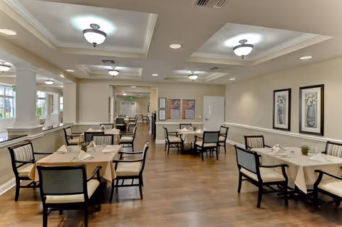 Well-lit dining room with multiple set tables and chairs on wood floors under recessed ceiling lights.