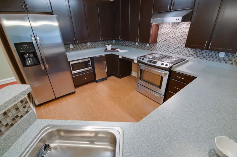 Modern kitchen with stainless steel refrigerator, stove and microwave, dark wood cabinets, mosaic tile backsplash, and a sink in the foreground.