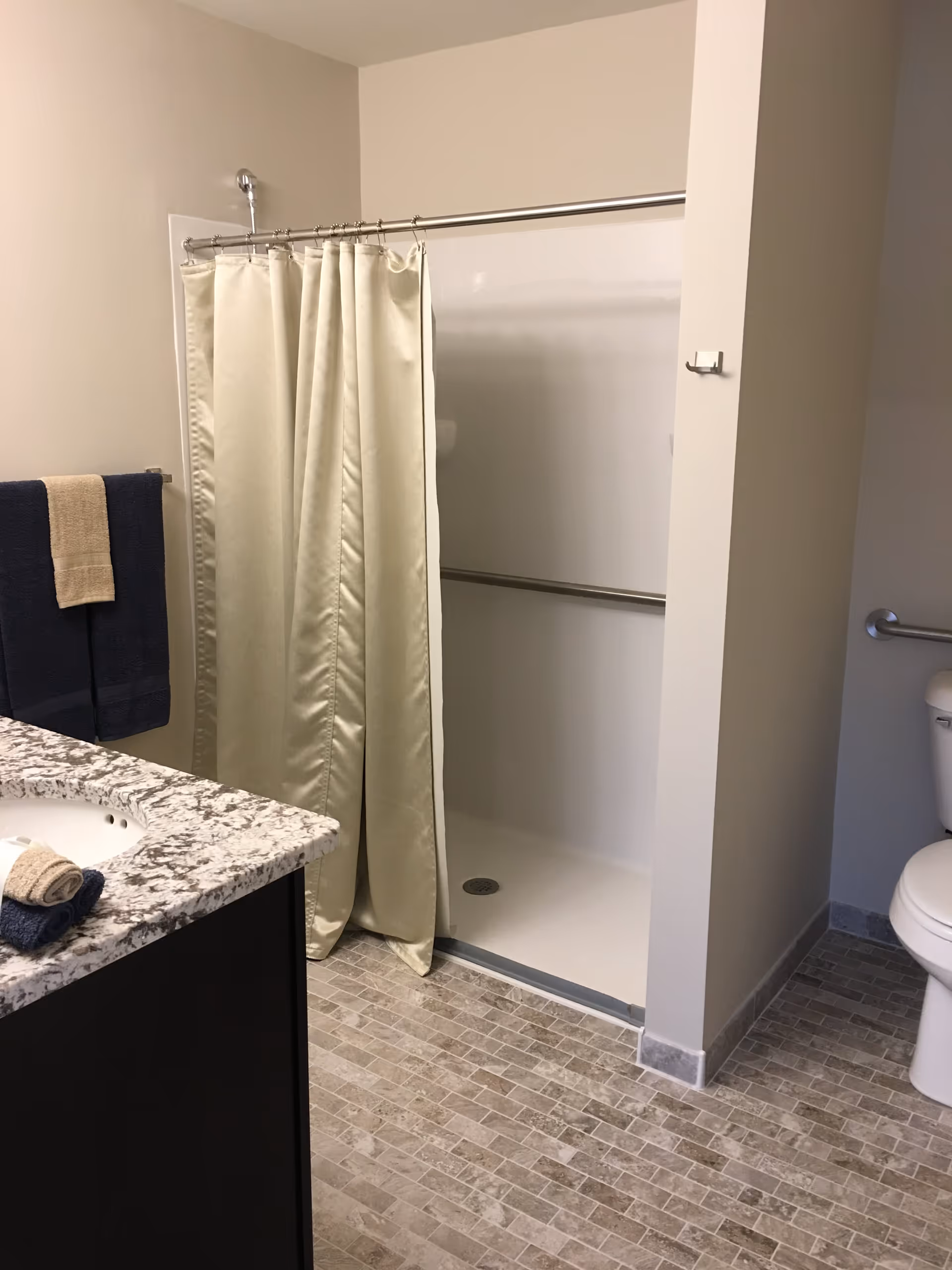 A bathroom featuring a walk-in shower with a beige curtain, granite countertop sink, towel rack, and toilet.