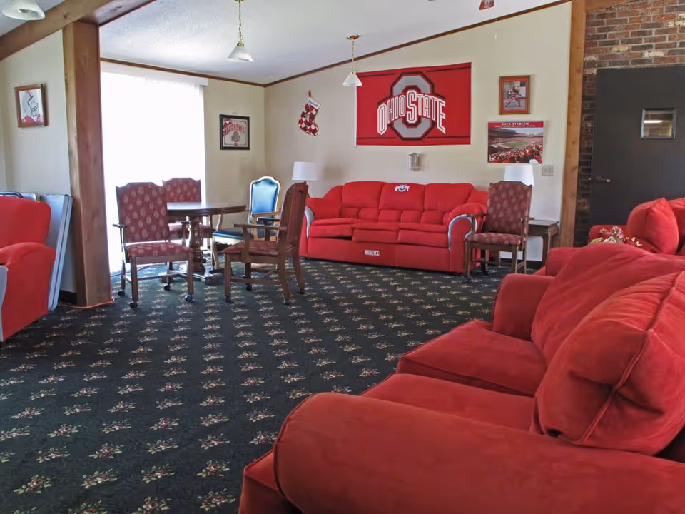 Communal lounge with red sofas and chairs, a small table with chairs, and an Ohio State banner on the wall.