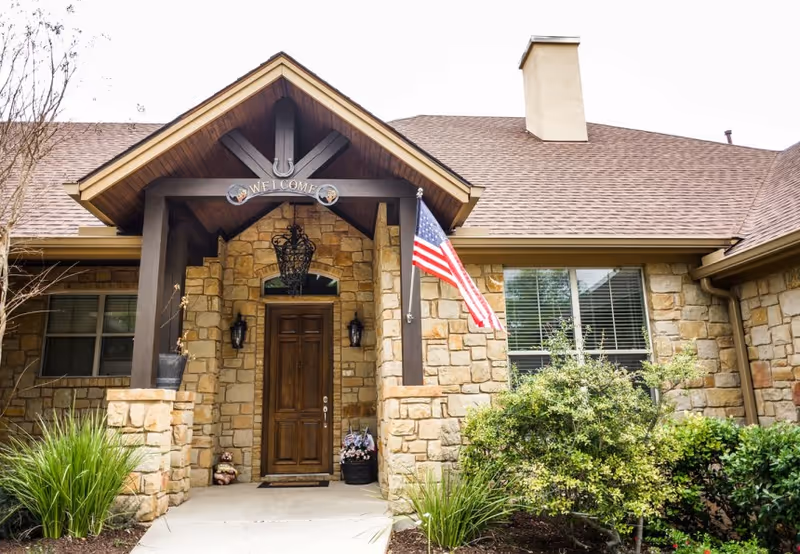 Stone-faced senior living facility entrance with wooden door and American flag