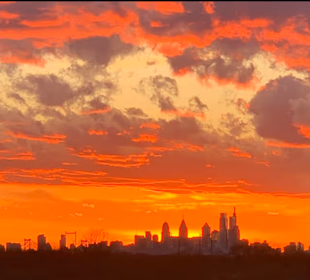 A vibrant sunset with orange and red hues lighting up the sky above a city skyline silhouette.