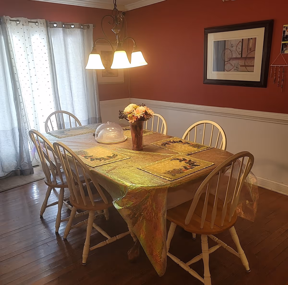 Dining room with a rectangular table set with placemats and a floral centerpiece, six wooden chairs, and an overhead light.