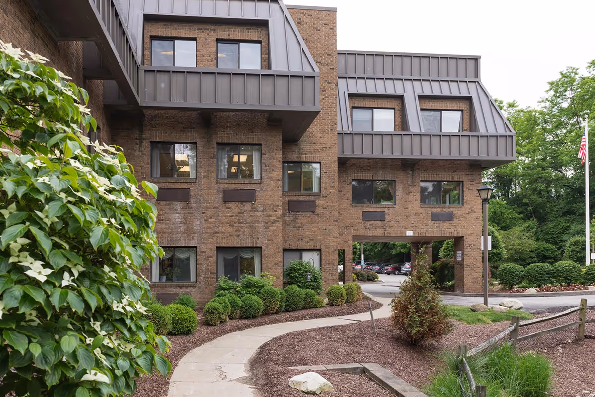 Exterior view of a multi-story brick senior living facility with balconies, a covered entrance, and landscaped walkways.