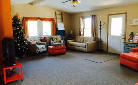 Cozy Rosewood Manor living room with sofas, red ottoman, Christmas tree, and windows.