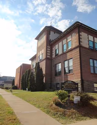 Brick senior living building with a sidewalk, sign, and manicured lawn under blue sky.