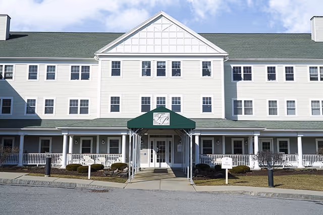 Front exterior of a three-story white senior living building with a green entry canopy and a covered porch.