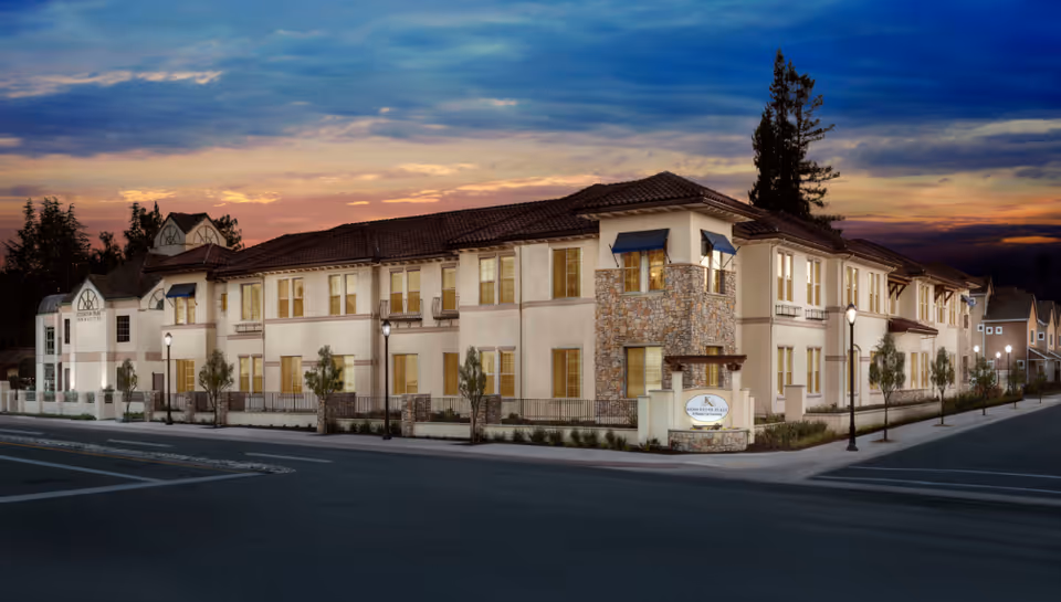 Two-story residential building at dusk with stone accents, awnings, and illuminated windows along a street.
