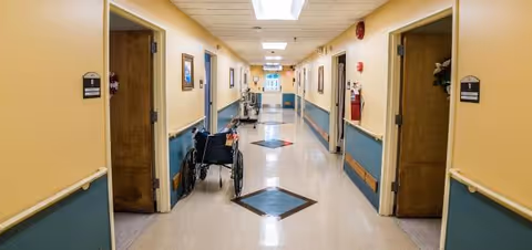 A long bright interior corridor at Laurel Manor with a wheelchair and doors.