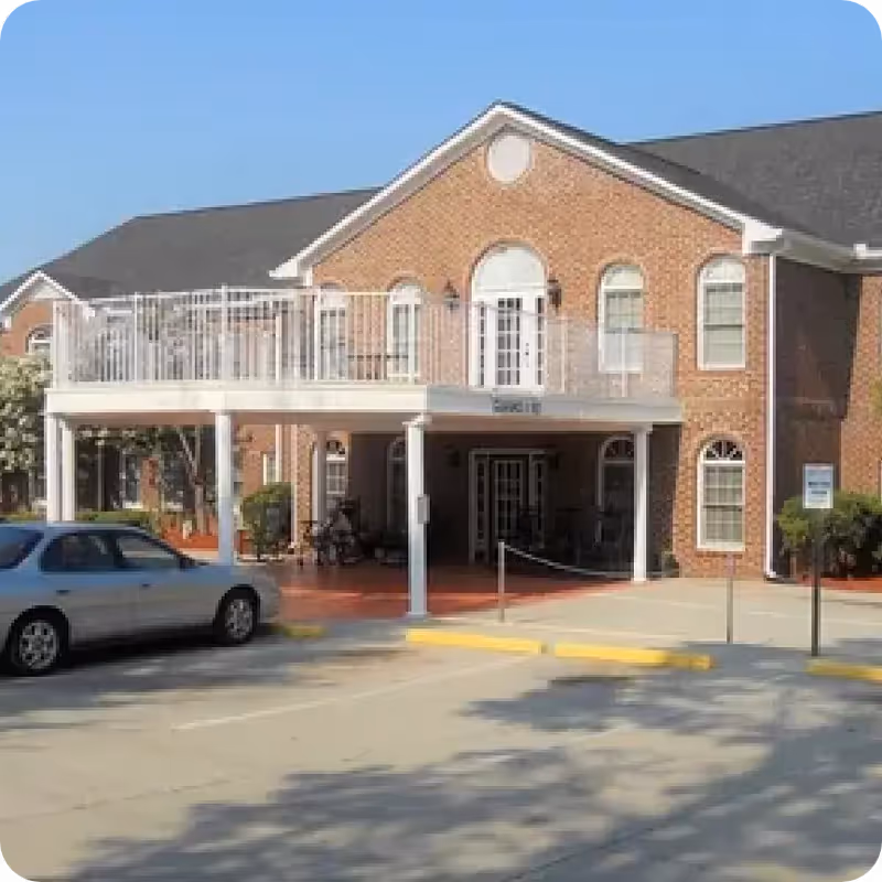 Front exterior of a brick senior living facility with a covered entrance and a second-floor balcony.