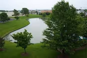 Landscaped pond surrounded by green grass and trees with buildings visible in the distance.