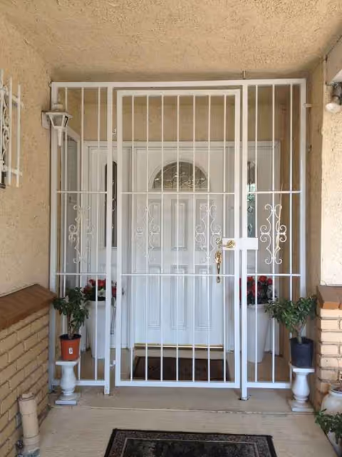 White metal security gate before a front door, flanked by potted plants.