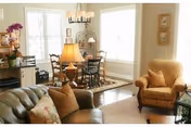 Bright open living room with a sofa and armchair leading into a dining area with a table and large windows.