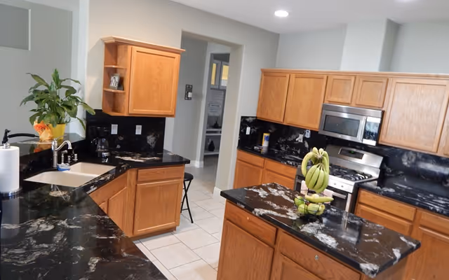 Modern kitchen with black marble countertops, oak cabinets, a center island, and stainless steel appliances.